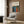 May include: Framed poster with colorful abstract art featuring flowing blue and red organic shapes with white and yellow dots on black background, displayed above beige upholstered armchair with geometric patterned pillow in modern living room setting with wood paneling, brass floor lamp, and side table