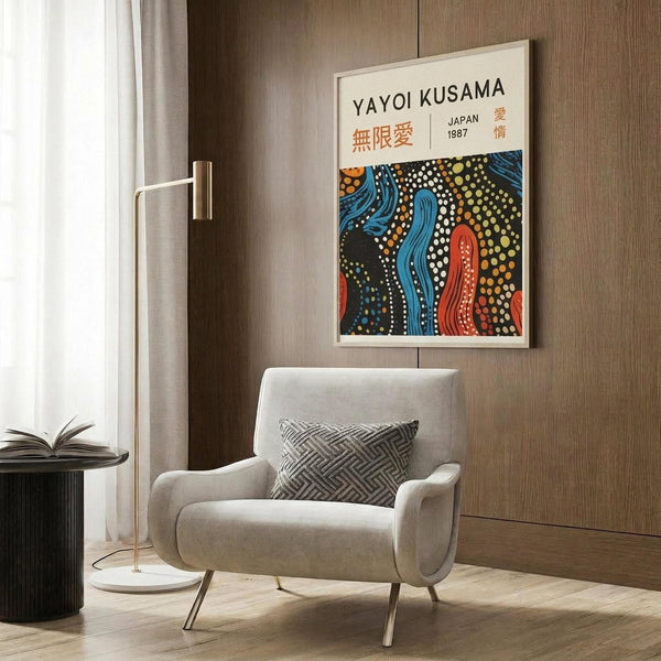 May include: Framed poster with colorful abstract art featuring flowing blue and red organic shapes with white and yellow dots on black background, displayed above beige upholstered armchair with geometric patterned pillow in modern living room setting with wood paneling, brass floor lamp, and side table