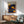 May include: Framed art print with blue background featuring yellow and orange polka dots and circular sun-like designs, displayed above a wooden credenza with white ceramic lamp in a mid-century modern living room setting with mint green upholstered chair and round coffee table