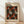 May include: Framed art print leaning against white wall on light wood floor with soft window light casting shadows. Black background poster features repeating pattern of red and white polka-dotted sculptural forms resembling pumpkins or shells, scattered with small yellow and white dots. Text reads "Yayoi Kusama" and "Infinity Shell" with Japanese characters and museum attribution. Natural wood frame with warm honey tone complements the cream-colored matting.