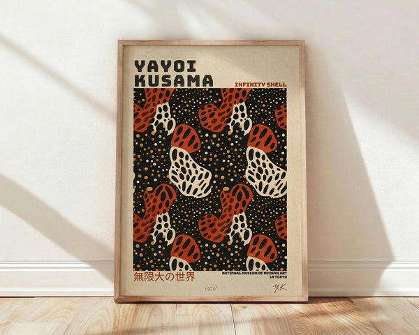 May include: Framed art print leaning against white wall on light wood floor with soft window light casting shadows. Black background poster features repeating pattern of red and white polka-dotted sculptural forms resembling pumpkins or shells, scattered with small yellow and white dots. Text reads "Yayoi Kusama" and "Infinity Shell" with Japanese characters and museum attribution. Natural wood frame with warm honey tone complements the cream-colored matting.
