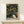 May include: Framed poster with abstract swirling design in dark green background featuring colorful polka dots in yellow, orange, red, and blue tones with flowing wave-like patterns. Text reads "YAYOI KUSAMA" with Japanese characters and "TOKYO" below. Light wood frame sits on pale wooden shelf against cream wall, creating modern minimalist display scene.
