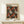 May include: Framed poster with black background featuring red and white polka-dotted mushroom pattern, displayed on light wood console table next to small wrapped gift with twine and greenery sprig against cream colored wall