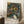 May include: Framed poster with colorful abstract design featuring swirling green patterns, scattered circles in yellow, orange, red, and white on dark background, with Japanese text and "TOKYO" at bottom. Light wood frame leaning against white wall next to coffee cup on wooden surface and cream blanket on textured rug.