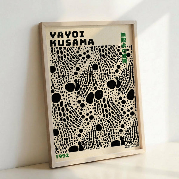A framed poster featuring black polka dots of varying sizes scattered across a cream background, creating Yayoi Kusama's signature infinity dot pattern. The artwork displays "YAYOI KUSAMA" in bold black letters at the top, with green text elements and "1992" in the corner. The poster is mounted in a light wood frame and photographed leaning against a white wall, showing the dimensional quality and neutral tones of this modern art print.