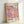 May include: Framed exhibition poster featuring colorful polka dot pattern in pink, purple, orange and cream circles of varying sizes. Light wood frame leaning against white wall. Japanese text at bottom reads "22 - APRIL 1986" and "無限の時間". Artist name "YAYOI KUSAMA" and "TOKYO 1998" printed at top, with "MUSÉE D'ART MODERNE DE LA VILLE DE PARIS" referenced below.
