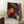 May include: Framed poster with abstract polka dot design in orange, pink, purple, and white circles on black background, displayed in light room corner next to coffee cup on wooden block and beige blanket on white furry rug.