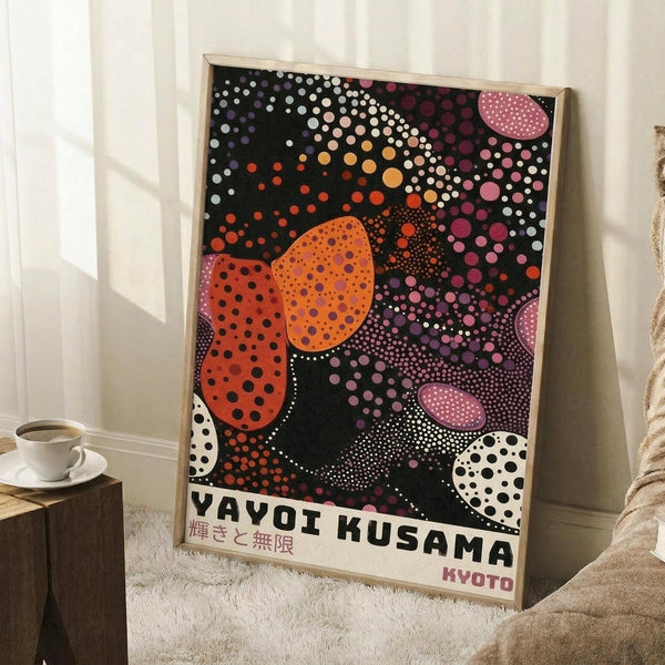 May include: Framed poster with abstract polka dot design in orange, pink, purple, and white circles on black background, displayed in light room corner next to coffee cup on wooden block and beige blanket on white furry rug.