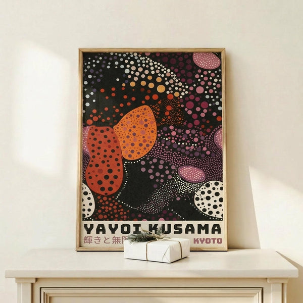 May include: Framed poster with colorful dotted abstract design in orange, pink, white and black polka dot patterns on dark background, displayed on light wood surface next to small wrapped gift box. Artwork features flowing organic shapes filled with various sized circles creating psychedelic visual effect. Natural lighting casts soft shadows on cream wall behind minimal wooden frame.