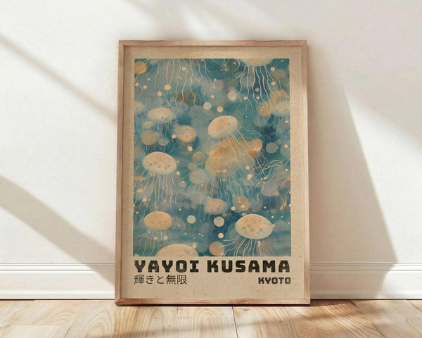 May include: Framed poster print featuring ethereal jellyfish floating in teal-blue water with flowing tentacles and circular spots, displayed in light wood frame against white textured wall on wooden floor. Japanese text at bottom reads "YAYOI KUSAMA" and "KYOTO" in dark letters. Soft natural lighting creates gentle shadows across the scene.