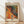 May include: Framed poster featuring Yayoi Kusama's distinctive polka dot artwork in vibrant oranges, yellows, and multicolored circular patterns against cream matting. Natural wood frame sits on light wooden floor against white wall with soft shadows from window light. The artwork shows flowing organic forms covered in signature infinity dots transitioning from warm tones to cooler blues and greens.