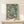 May include: Framed poster with jellyfish floating in turquoise water, featuring flowing tentacles and circular bubble patterns in cream and peach tones. Text reads "Yayoi Kusama" and "Kyoto" at bottom. Natural wood frame sits on light wooden surface beside small white wrapped gift with evergreen sprig against cream wall.