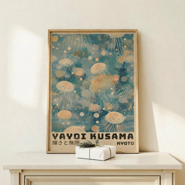 May include: Framed poster with jellyfish floating in turquoise water, featuring flowing tentacles and circular bubble patterns in cream and peach tones. Text reads "Yayoi Kusama" and "Kyoto" at bottom. Natural wood frame sits on light wooden surface beside small white wrapped gift with evergreen sprig against cream wall.