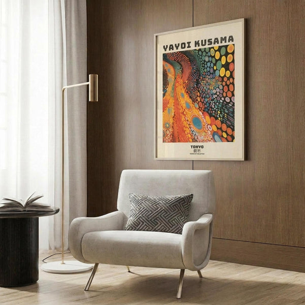 May include: Colorful abstract art poster with orange, green, and multicolored dotted pattern hanging on wood-paneled wall above beige upholstered armchair with geometric pillow. Gold floor lamp and dark side table with open book nearby. Modern minimalist interior with warm wood tones and natural lighting from window with white curtains.