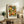 May include: Framed art print featuring colorful circular and floral patterns in orange, green, yellow, and white dots displayed on a wooden sideboard next to a fern plant, ceramic vase, and books in a neutral-toned living room setting with beige furniture.