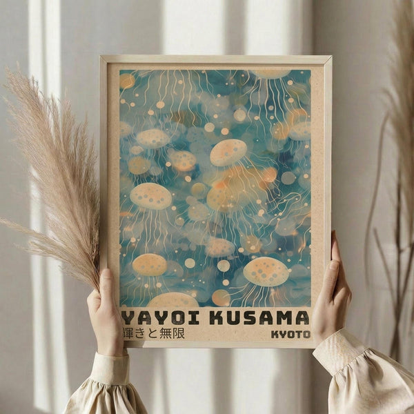 May include: Person in cream sweater holding framed poster featuring jellyfish floating in teal-blue water with flowing tentacles and spots in warm beige tones. Light wooden frame against white curtained window with dried pampas grass. Japanese text visible at bottom of vintage-style travel poster design.