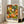 May include: Framed poster with colorful polka dot artwork in vibrant oranges, greens, yellows, and white against black background, featuring circular flower-like patterns and dots in Kusama's signature style. Text reads "YAYOI KUSAMA" with Japanese characters and "NAGOYA" below. Light wood frame leaning against white wall next to beige upholstered chair in bright room with large windows.