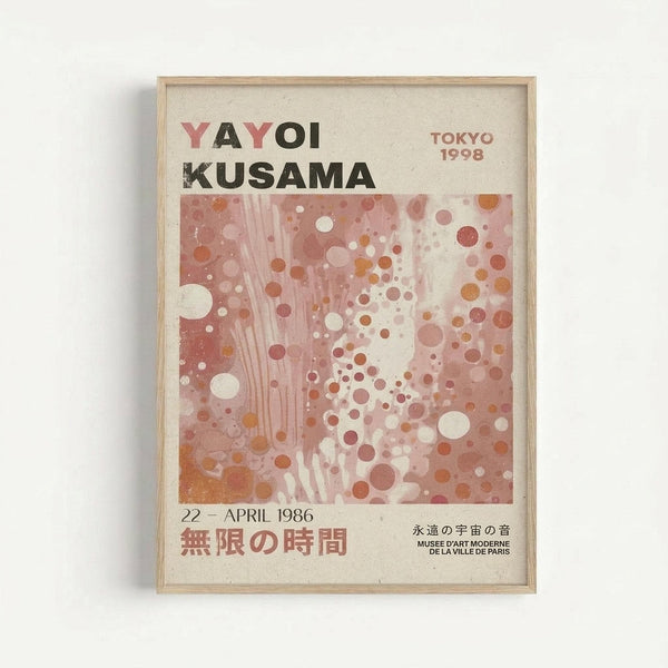 A framed exhibition poster featuring Yayoi Kusama's name in bold black and pink letters at the top, with "TOKYO 1998" in smaller text. The main artwork shows an abstract composition of polka dots in various sizes and warm tones of pink, coral, orange and cream against a soft background. Below the artwork is "22 - APRIL 1986" and Japanese characters, with museum credit text at the bottom. The poster is displayed in a light wooden frame against a white wall.
