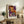 May include: Framed colorful abstract art print with orange, purple, and black polka dot patterns displayed on wooden console table beside fern plant, ceramic vase, and books in modern living room setting with beige armchair