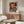 May include: Colorful abstract art poster with vibrant orange, purple, and cream circular patterns and dots, displayed in light wood frame above mid-century modern walnut credenza. Modern living room setting features white sculptural chair, glass-top oval coffee table, and minimalist table lamps. Warm natural lighting creates soft shadows on neutral walls.