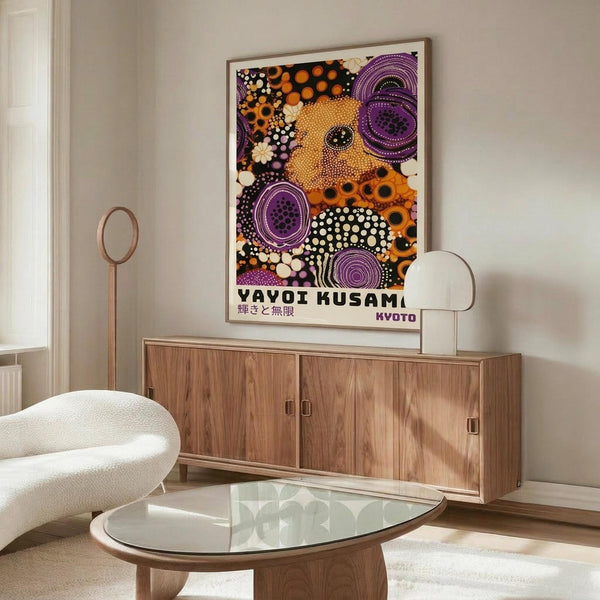 May include: Colorful abstract art poster with vibrant orange, purple, and cream circular patterns and dots, displayed in light wood frame above mid-century modern walnut credenza. Modern living room setting features white sculptural chair, glass-top oval coffee table, and minimalist table lamps. Warm natural lighting creates soft shadows on neutral walls.