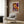 May include: Colorful poster featuring abstract circular patterns in orange, purple, and white with dotted textures, hung in light wood frame on wood-paneled wall above modern beige armchair with geometric throw pillow, brass floor lamp and dark side table with open book nearby