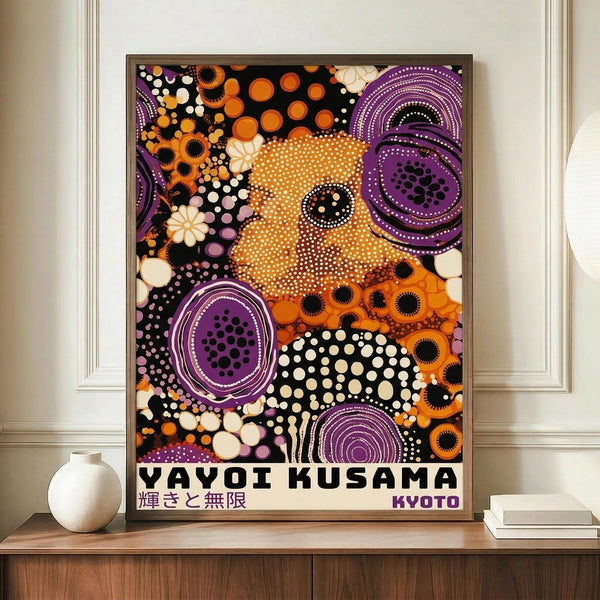 May include: Framed poster with colorful abstract dot artwork featuring orange, purple, black and white circular patterns, displayed on wooden sideboard next to white ceramic vase and stacked books against cream wall with white molding.