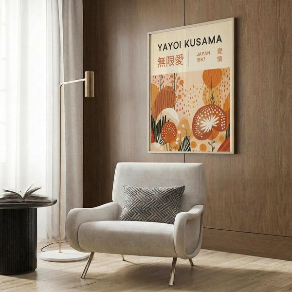 May include: Framed vintage-style art poster with orange and cream botanical design featuring abstract flowers and Japanese text, displayed on wood paneled wall above beige upholstered armchair with geometric patterned pillow, beside brass floor lamp and dark round side table with open book
