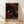 May include: Framed poster with black background featuring scattered polka dots in orange, cream, and rust tones of varying sizes, some forming constellation-like patterns. Text reads "YAYOI KUSAMA" with Japanese characters and "TOKYO" below. Natural wood frame sits against white wall on light wooden floor with soft shadows.