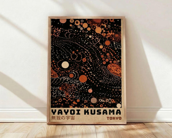 May include: Framed poster with black background featuring scattered polka dots in orange, cream, and rust tones of varying sizes, some forming constellation-like patterns. Text reads "YAYOI KUSAMA" with Japanese characters and "TOKYO" below. Natural wood frame sits against white wall on light wooden floor with soft shadows.