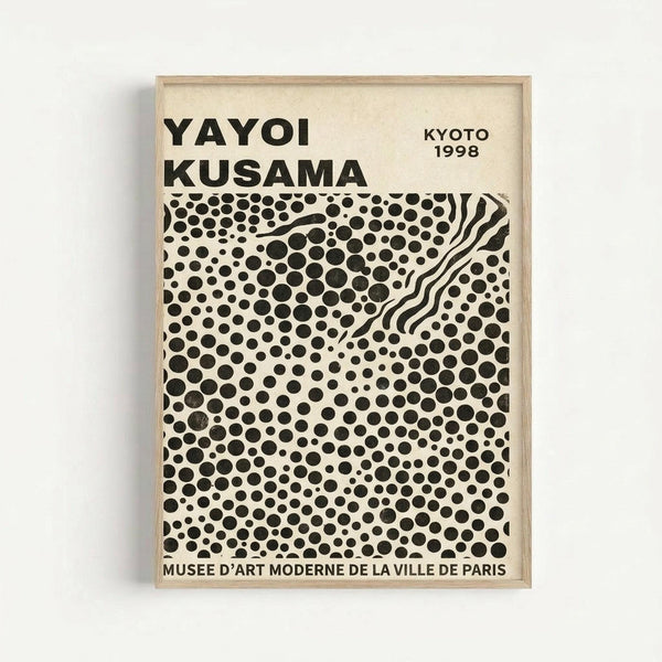 A framed exhibition poster featuring black polka dots of varying sizes scattered across a cream background, with wavy white lines cutting through the dot pattern in the upper right. Bold black text reads "YAYOI KUSAMA" at the top left, "KYOTO 1998" at the top right, and "MUSEE D'ART MODERNE DE LA VILLE DE PARIS" at the bottom. The poster is displayed in a light wooden frame against a white wall.