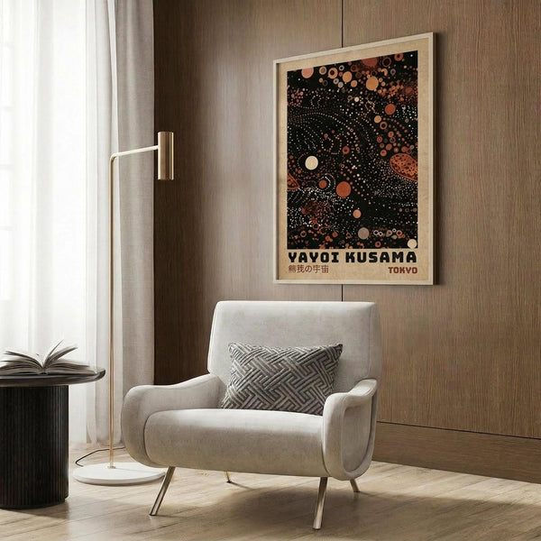 May include: Framed art print with black background featuring colorful dots and circles in orange, coral, and cream tones with dotted spiral patterns, displayed on wood-paneled wall above beige upholstered chair with geometric pillow, next to gold floor lamp and side table with open book in modern living room setting.