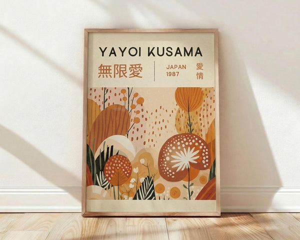May include: Framed poster with cream background featuring "YAYOI KUSAMA" text and Japanese characters, displaying abstract botanical illustration in warm orange, brown, and cream tones with stylized flowers, leaves, and dotted patterns. Wood frame leaning against white wall on light wooden floor with natural sunlight casting shadows.