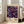 May include: Framed vintage exhibition poster featuring colorful abstract flowers in purple, pink, blue, and orange tones against dark background with scattered dots, displayed on light wooden floor next to beige sofa in bright room with white walls and large windows