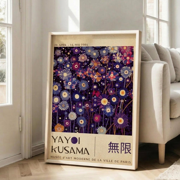 May include: Framed vintage exhibition poster featuring colorful abstract flowers in purple, pink, blue, and orange tones against dark background with scattered dots, displayed on light wooden floor next to beige sofa in bright room with white walls and large windows