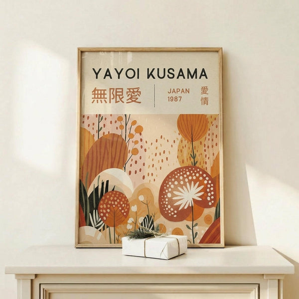 May include: Framed art print displaying "YAYOI KUSAMA" text at top with Japanese characters and "JAPAN 1987" below. Abstract botanical illustration features warm orange, rust, and cream colored organic shapes, polka-dotted mushrooms, stylized plants and flowers in mid-century modern style. Natural wood frame sits on light wooden surface against cream wall with small wrapped gift box nearby.