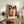 May include: Framed cubist-style portrait print displaying geometric face with orange and brown color blocks, asymmetrical eyes, and angular features in wooden frame. Print sits on rustic wooden sideboard alongside potted fern, ceramic vase, and stacked books in warm-toned living room setting with cream upholstered furniture.