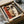 May include: Cubist-style portrait print in cardboard shipping box with protective packaging. Abstract face features geometric shapes in warm tones of red, orange, brown and cream. Two wooden poster tubes wrapped in plastic lie beside the opened package on white tissue paper. Black picture frame visible underneath print.