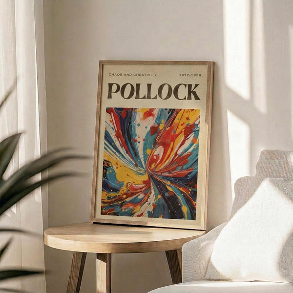 a framed poster of a colorful abstract painting, which is leaning against a wall in a room with a wooden table and a white chair.