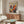 a living room with a large abstract painting hanging on the wall above a wooden cabinet. The painting has a vibrant, colorful design with swirling patterns and shapes. The room also includes a white sofa, a glass coffee table, and a lamp on a side table.