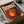 a framed poster or artwork with a vibrant, abstract design featuring a large sun-like shape in shades of red, orange, and yellow, surrounded by splashes of black and white. The poster is placed in a cardboard box, which is wrapped in bubble wrap.