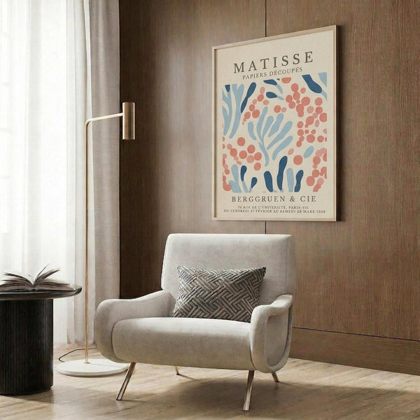 a living room with a white armchair, a floor lamp, and a framed poster of the Métisse artists' work hanging on the wall.