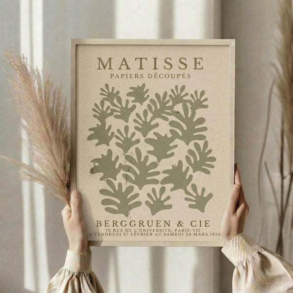 A person's hands holding a framed poster with a design of green leaf-like shapes.