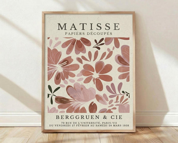The image is a poster for the painting "Matisse: Papiers Decoupes" by the artist Berg Gruen & Cie. The poster features a floral pattern in shades of pink and brown, and it is displayed on a wooden floor against a white wall.
