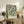 a framed poster of a green and white floral pattern, placed on a wooden cabinet or shelf in a room with a lamp and other decorative items.