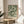 a framed poster of a floral pattern on a wall, placed on a small round table in a room with a white chair and a plant in the background.