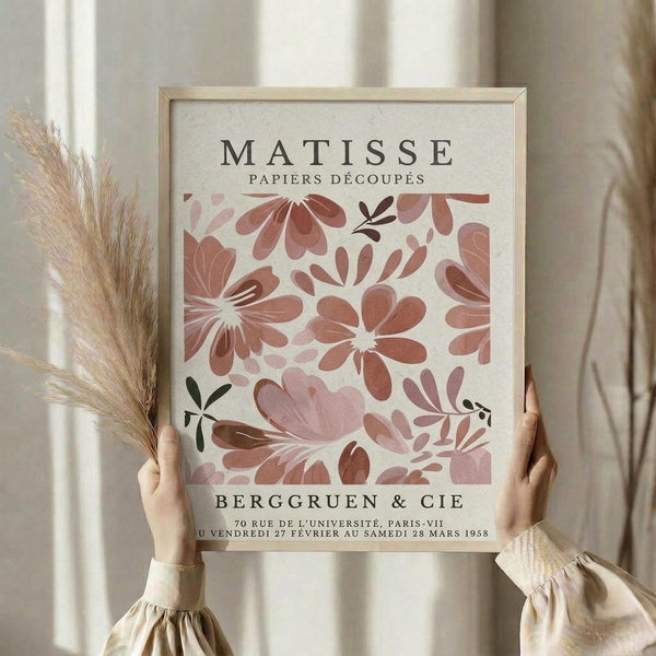 A person is holding up a framed poster of the work "MATISSE Papiers Decoupes" by the artist Berg Gruen, which features a floral pattern in shades of pink and red.