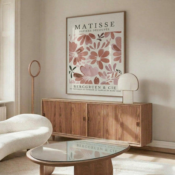 a living room with a large poster of the painting "Matsisse" hanging on the wall above a wooden cabinet. The cabinet has a glass top, and there is a white sofa in the room.