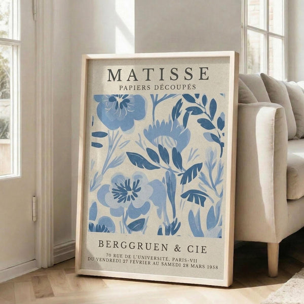 A framed poster of the M.C. Escher's "Matisse" artwork, featuring a blue floral pattern, is displayed on a wooden floor in front of a couch.