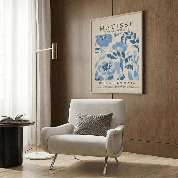 a living room with a white armchair, a floor lamp, and a framed poster of the Métisse painting "Papiers D'ocuples" hanging on the wall.